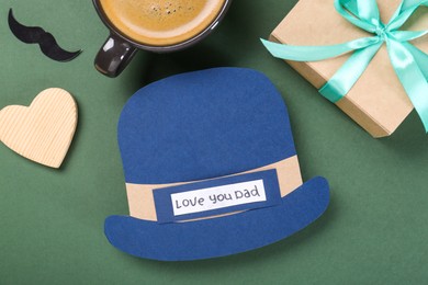 Photo of Happy Father's Day. Paper hat, cup of coffee, moustache, gift box and heart on green background, flat lay