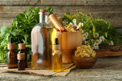 Photo of Tinctures in bottles, medicinal herbs and mortar with pestle on wooden table