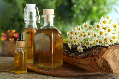 Photo of Different tinctures in bottles and chamomile flowers on wooden table