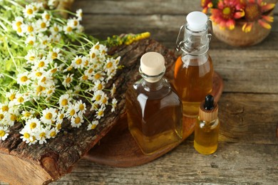 Photo of Different tinctures in bottles and chamomile flowers on wooden table