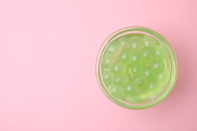 Photo of Bright tapioca pearls in bowl on pink background, top view. Space for text