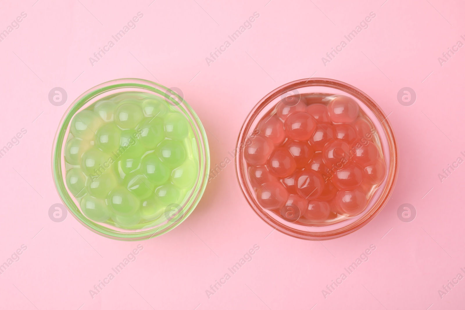 Photo of Bright tapioca pearls in bowls on pink background, flat lay