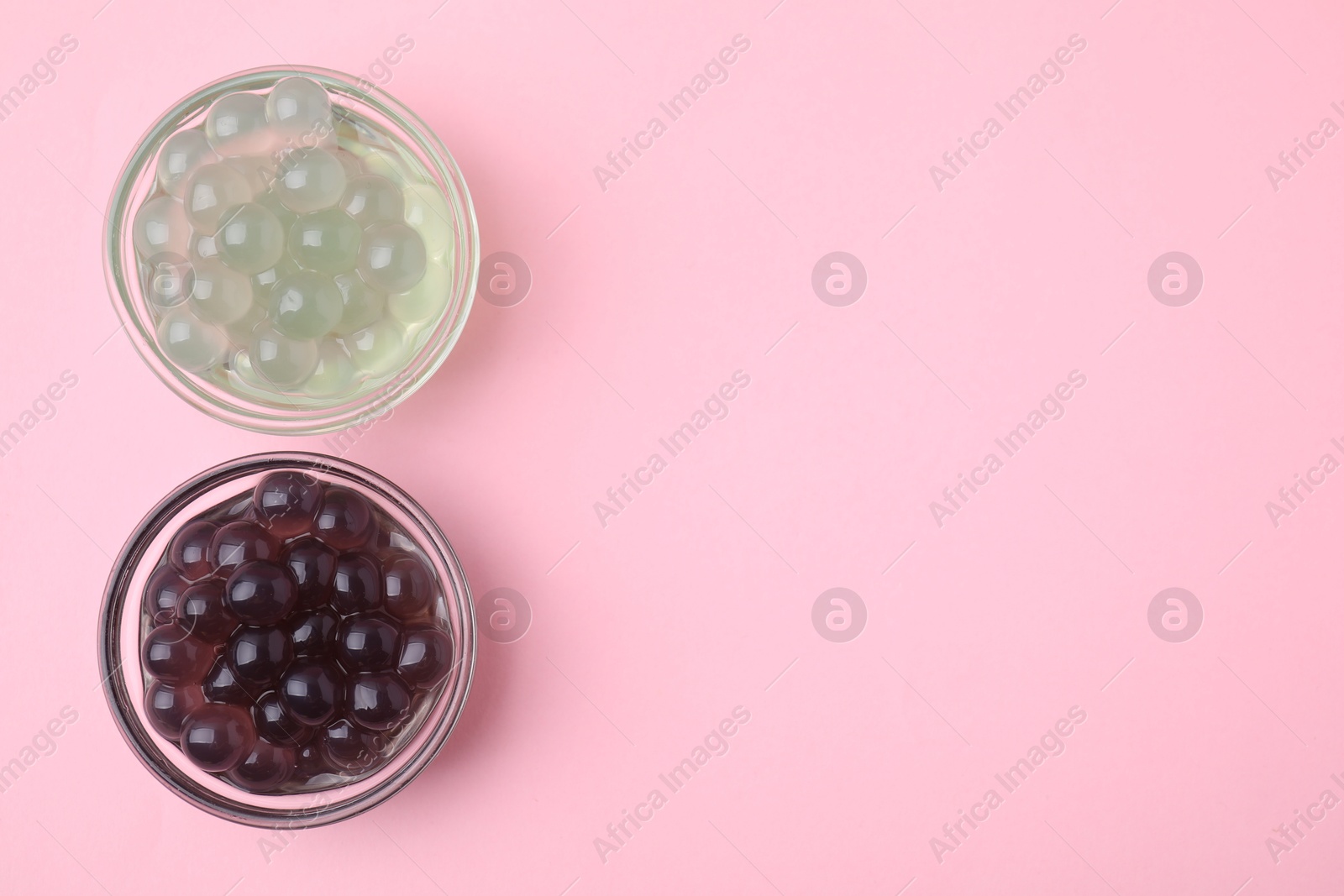 Photo of Color tapioca pearls in bowls on pink background, flat lay. Space for text