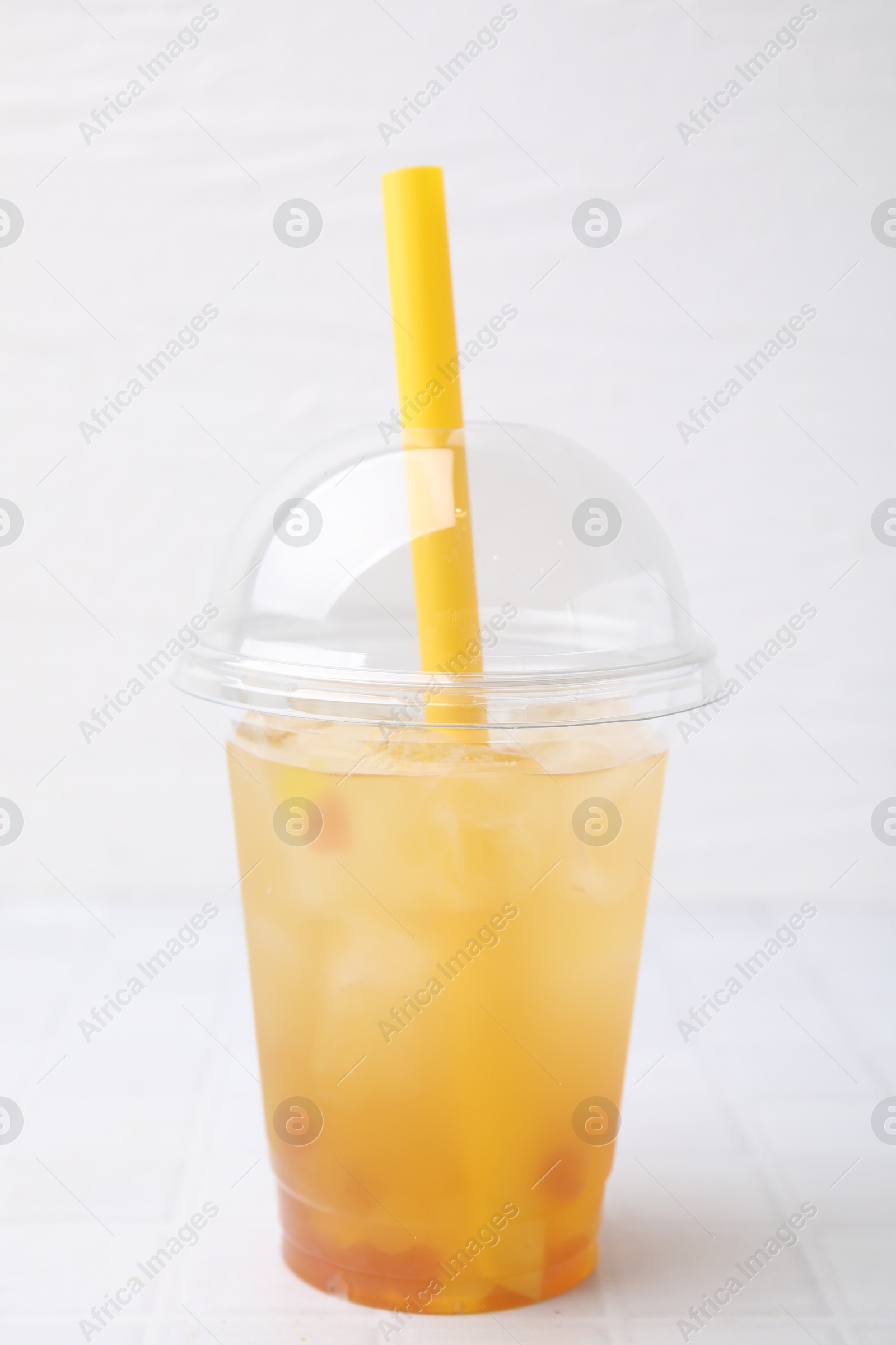 Photo of Tasty bubble tea in plastic cup on white tiled table against light background