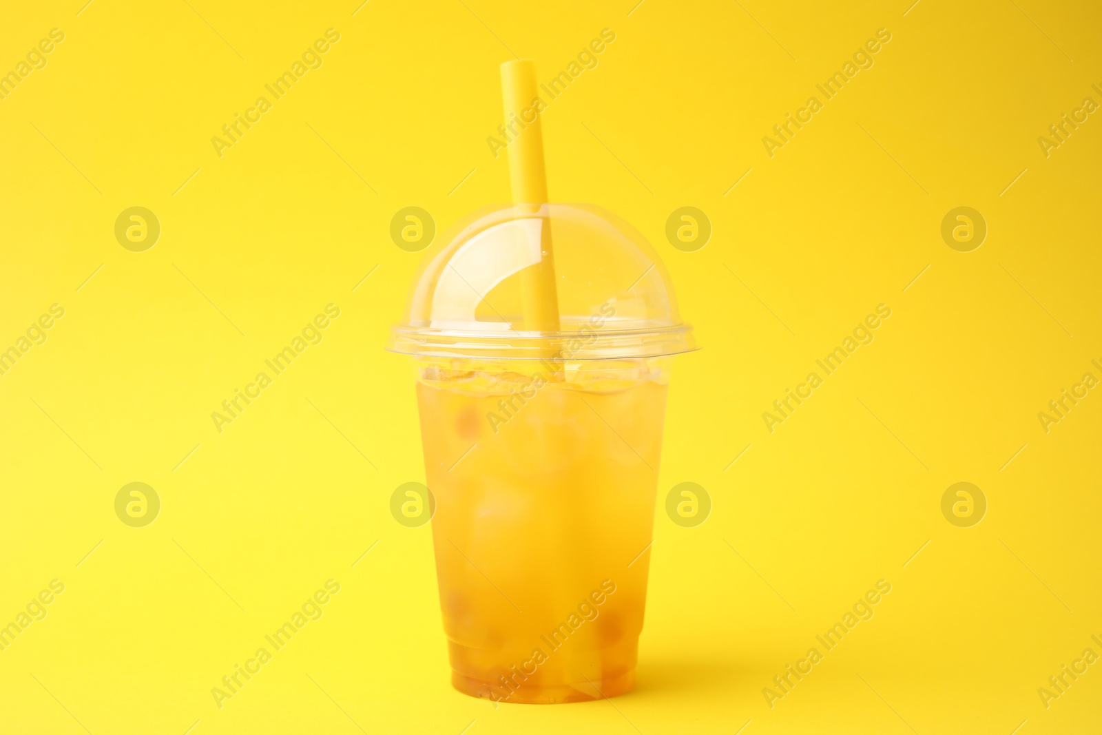 Photo of Tasty bubble tea in plastic cup on yellow background