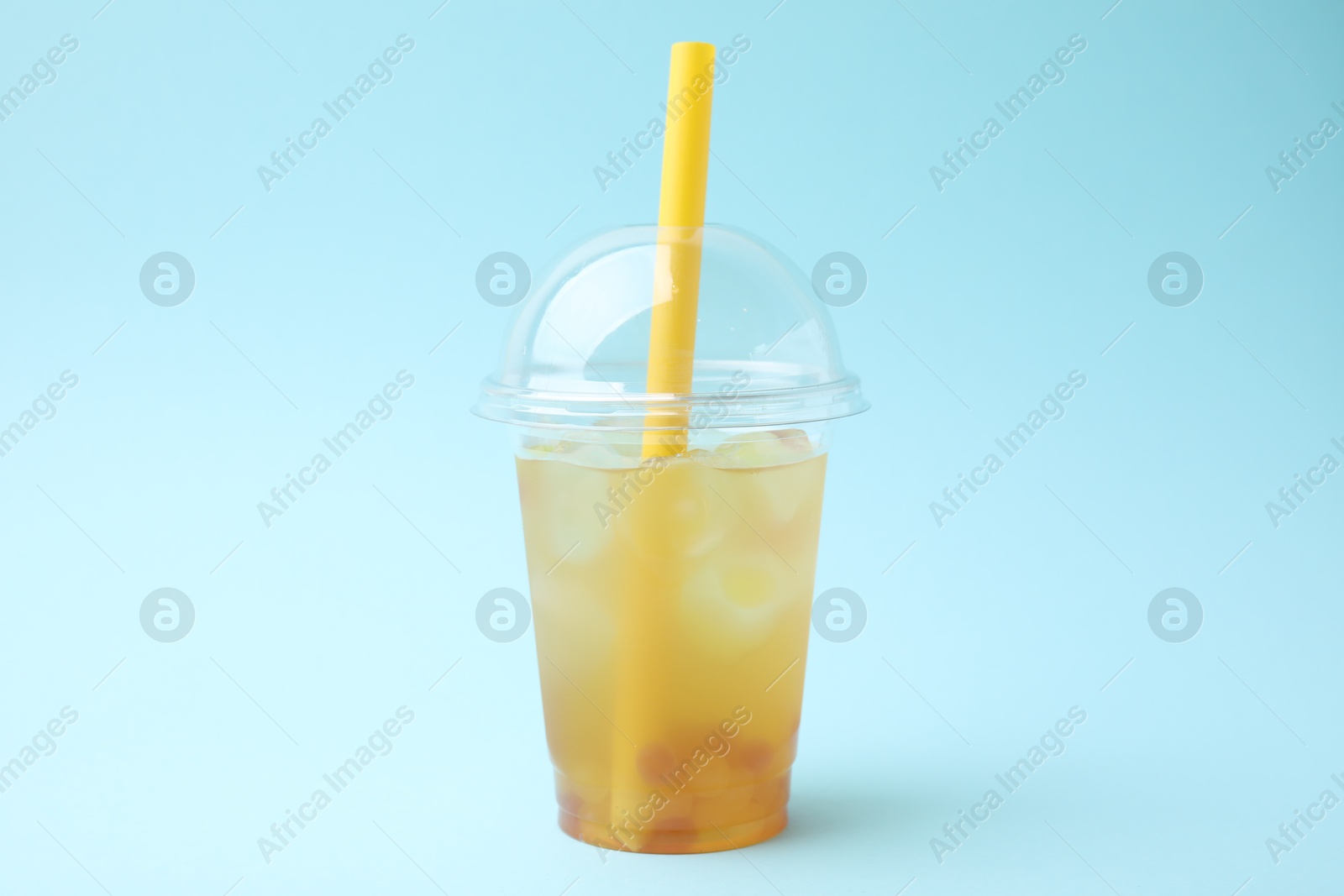 Photo of Tasty bubble tea in plastic cup on light blue background