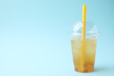 Photo of Tasty bubble tea in plastic cup on light blue background, space for text