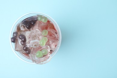 Photo of Tasty bubble tea in plastic cup on light blue background, top view. Space for text