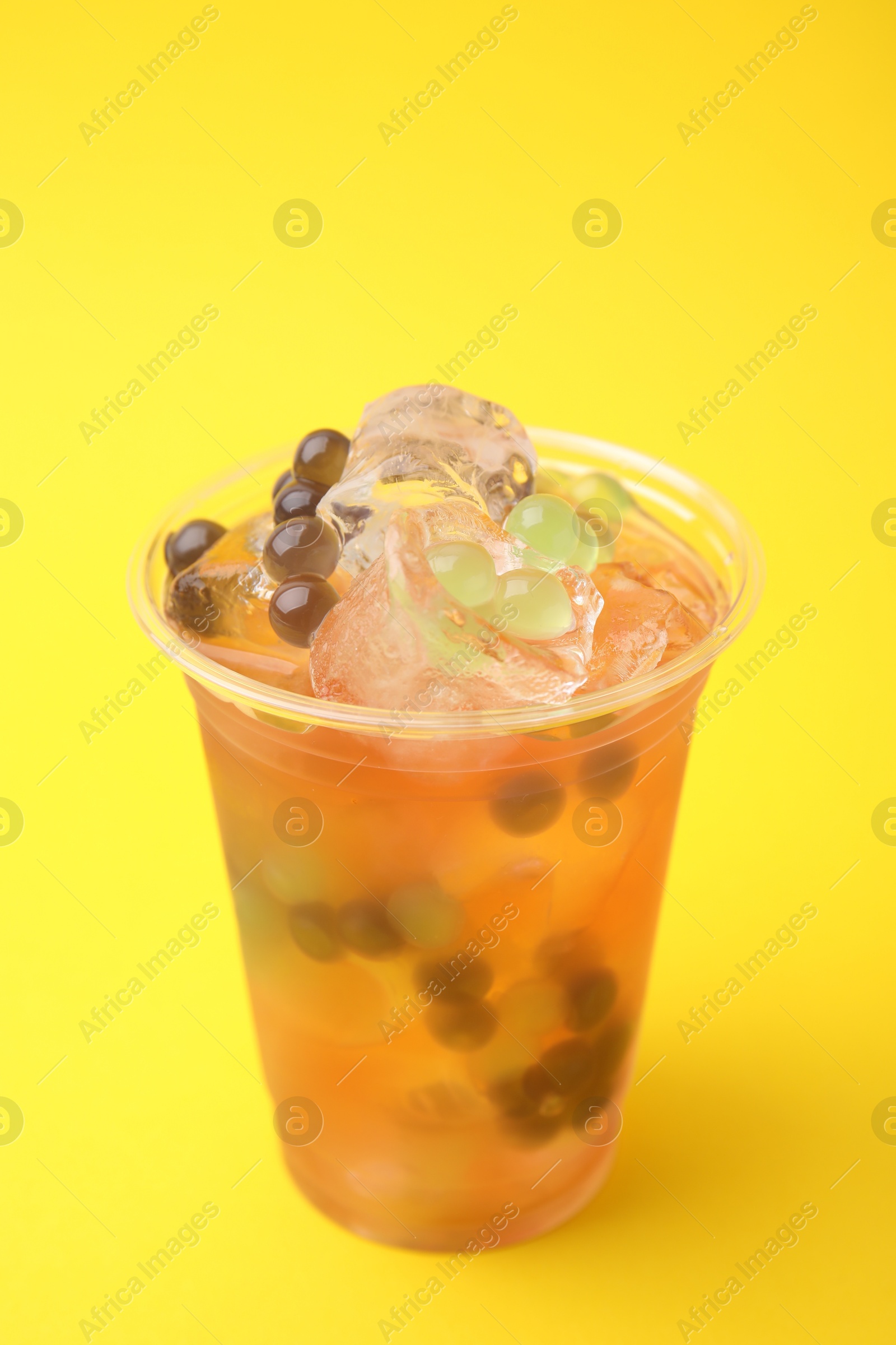 Photo of Tasty bubble tea in plastic cup on yellow background