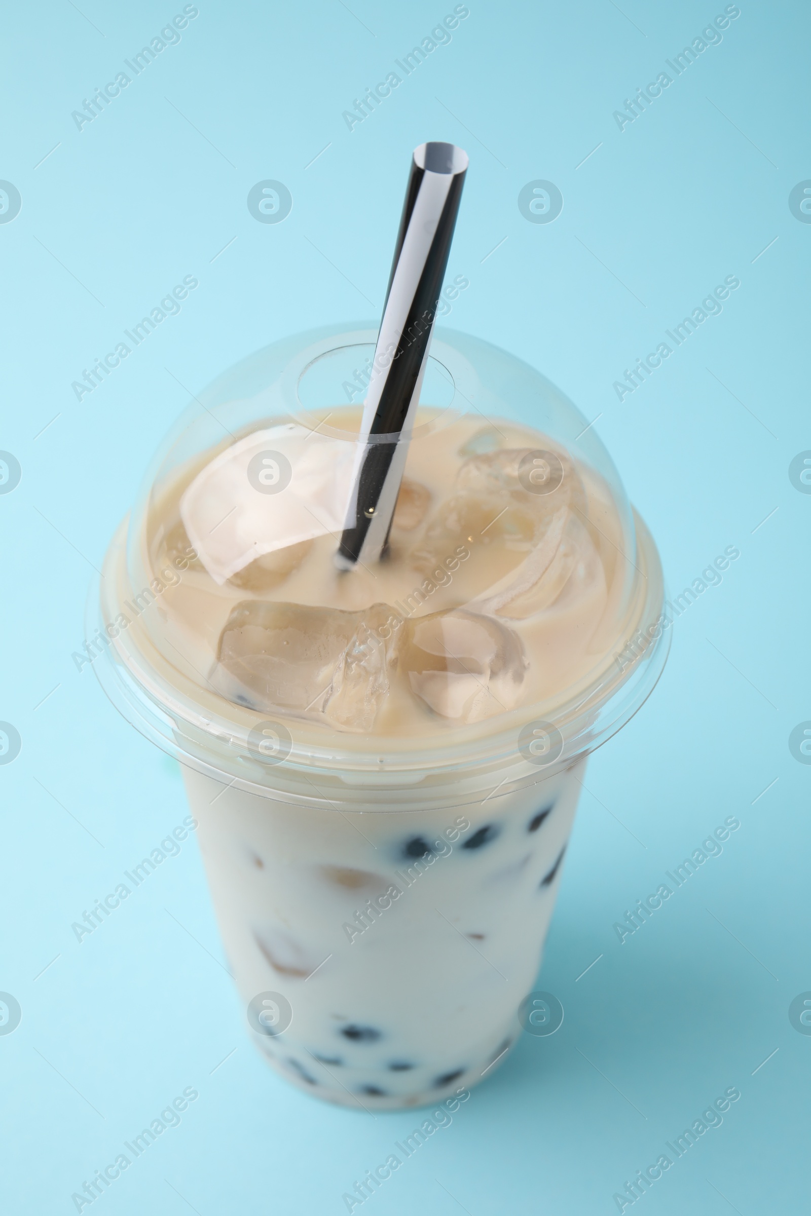 Photo of Tasty milk bubble tea in plastic cup on light blue background, closeup