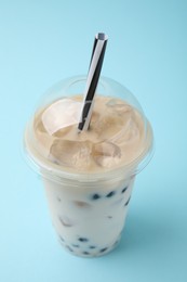 Tasty milk bubble tea in plastic cup on light blue background, closeup