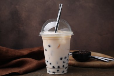 Photo of Tasty milk bubble tea in plastic cup on wooden table against brown background