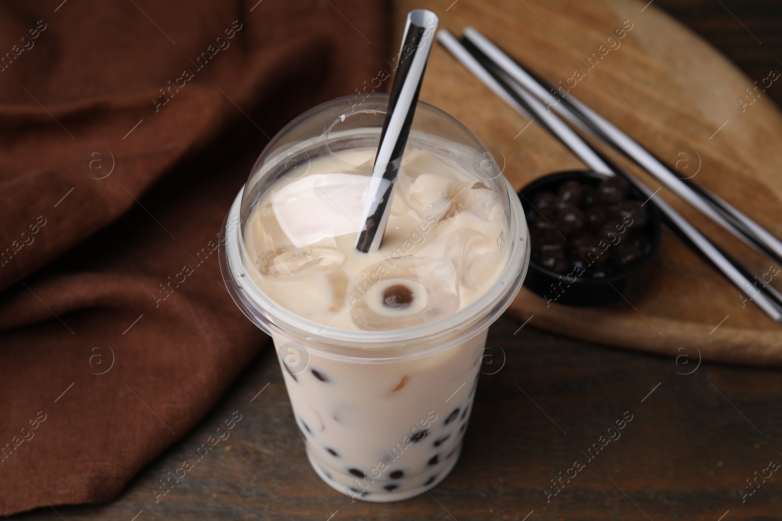 Photo of Tasty milk bubble tea in plastic cup on wooden table, closeup