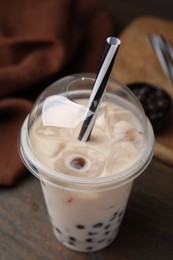 Photo of Tasty milk bubble tea in plastic cup on wooden table, closeup