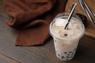 Tasty milk bubble tea in plastic cup on wooden table, closeup