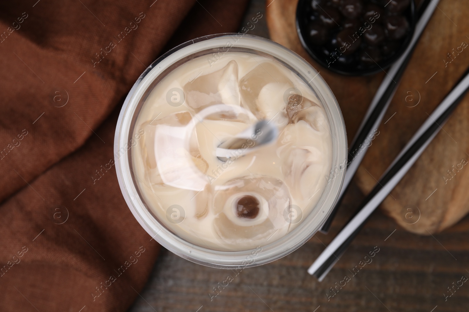 Photo of Tasty milk bubble tea in plastic cup, tapioca pearls and straws on wooden table, flat lay