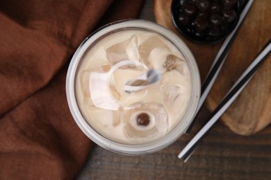 Tasty milk bubble tea in plastic cup, tapioca pearls and straws on wooden table, flat lay