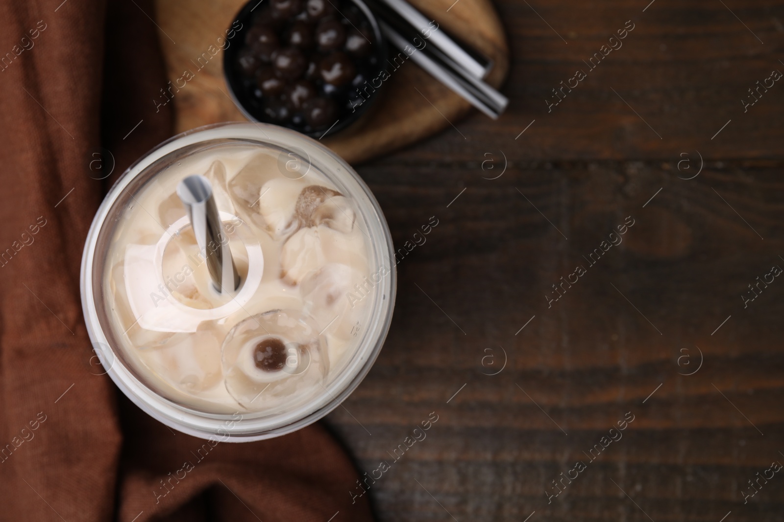 Photo of Tasty milk bubble tea in plastic cup, tapioca pearls and straws on wooden table, flat lay. Space for text