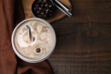 Tasty milk bubble tea in plastic cup, tapioca pearls and straws on wooden table, flat lay. Space for text