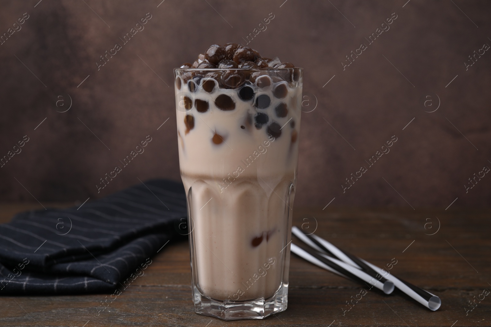 Photo of Tasty milk bubble tea in glass on wooden table against brown background