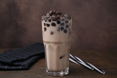 Photo of Tasty milk bubble tea in glass on wooden table against brown background