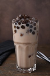 Photo of Tasty milk bubble tea in glass on wooden table against brown background