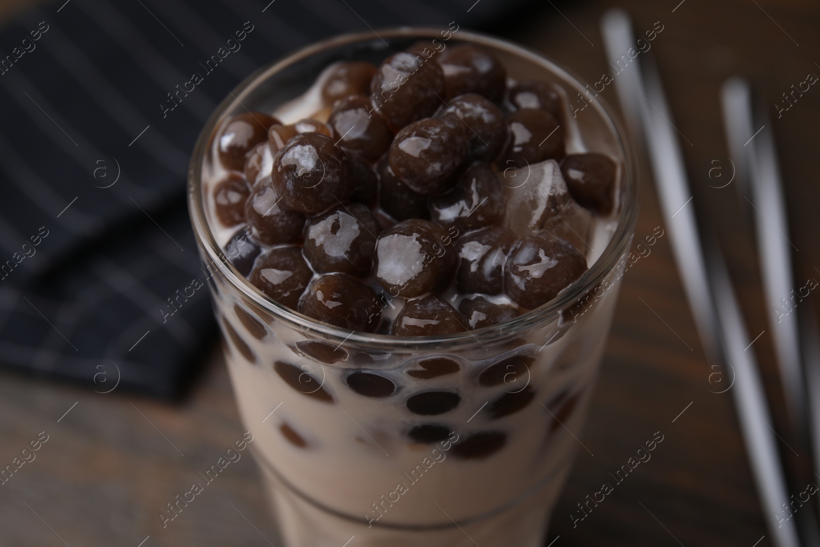 Photo of Tasty milk bubble tea in glass on brown table, closeup