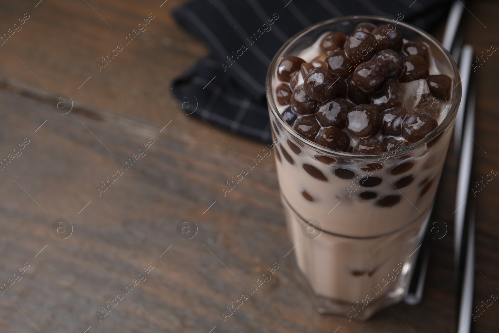 Photo of Tasty milk bubble tea in glass on wooden table, closeup. Space for text