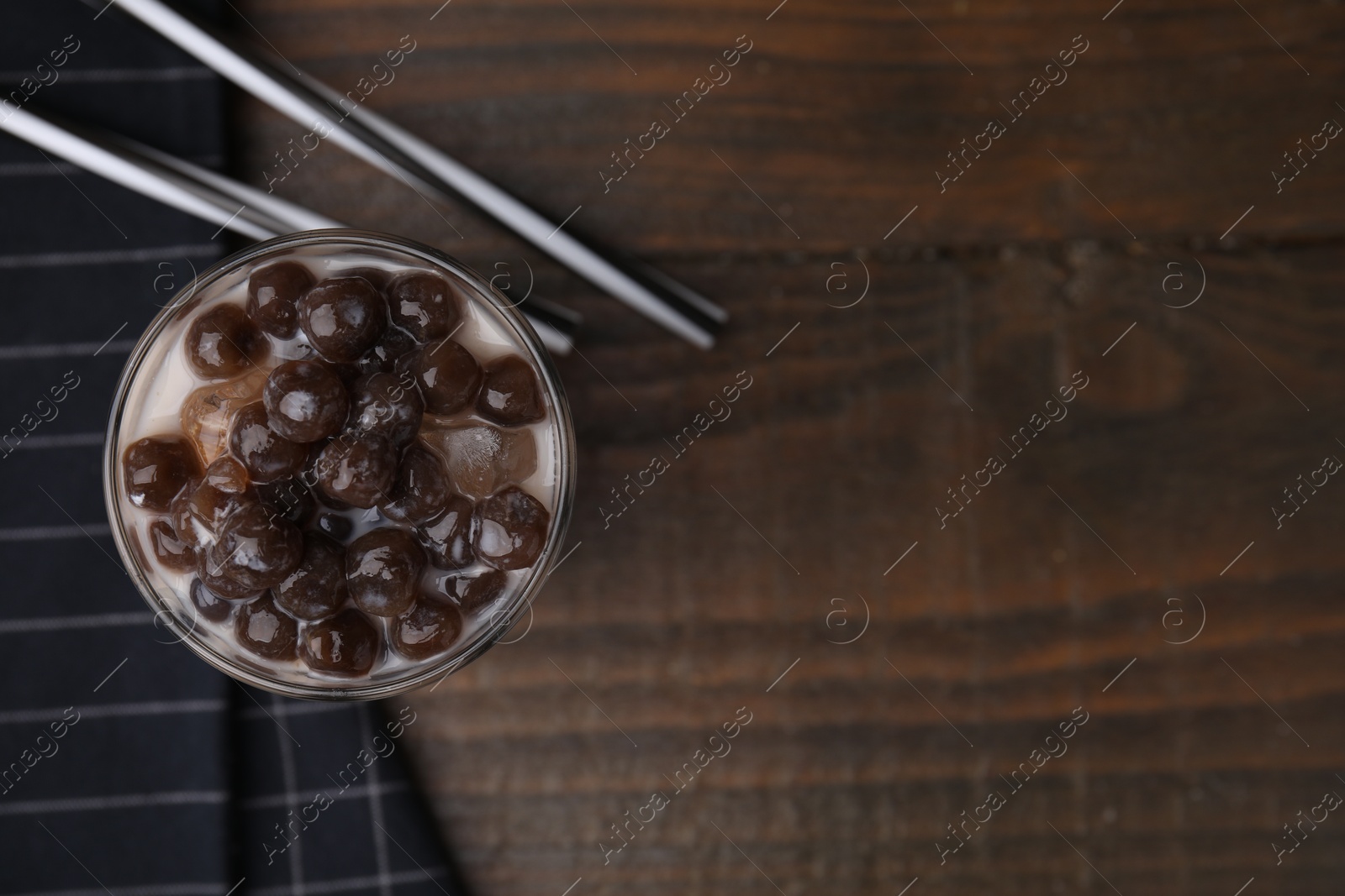 Photo of Tasty milk bubble tea in glass and straws on wooden table, flat lay. Space for text