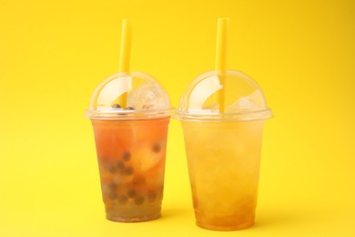 Photo of Tasty bubble tea in plastic cups on yellow background