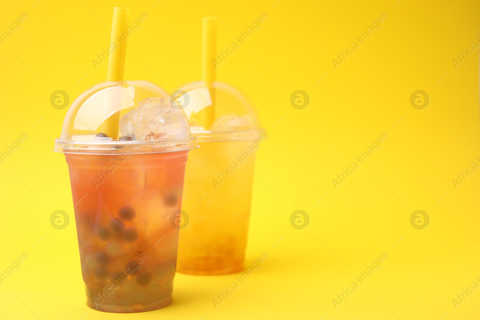 Photo of Tasty bubble tea in plastic cups on yellow background, space for text