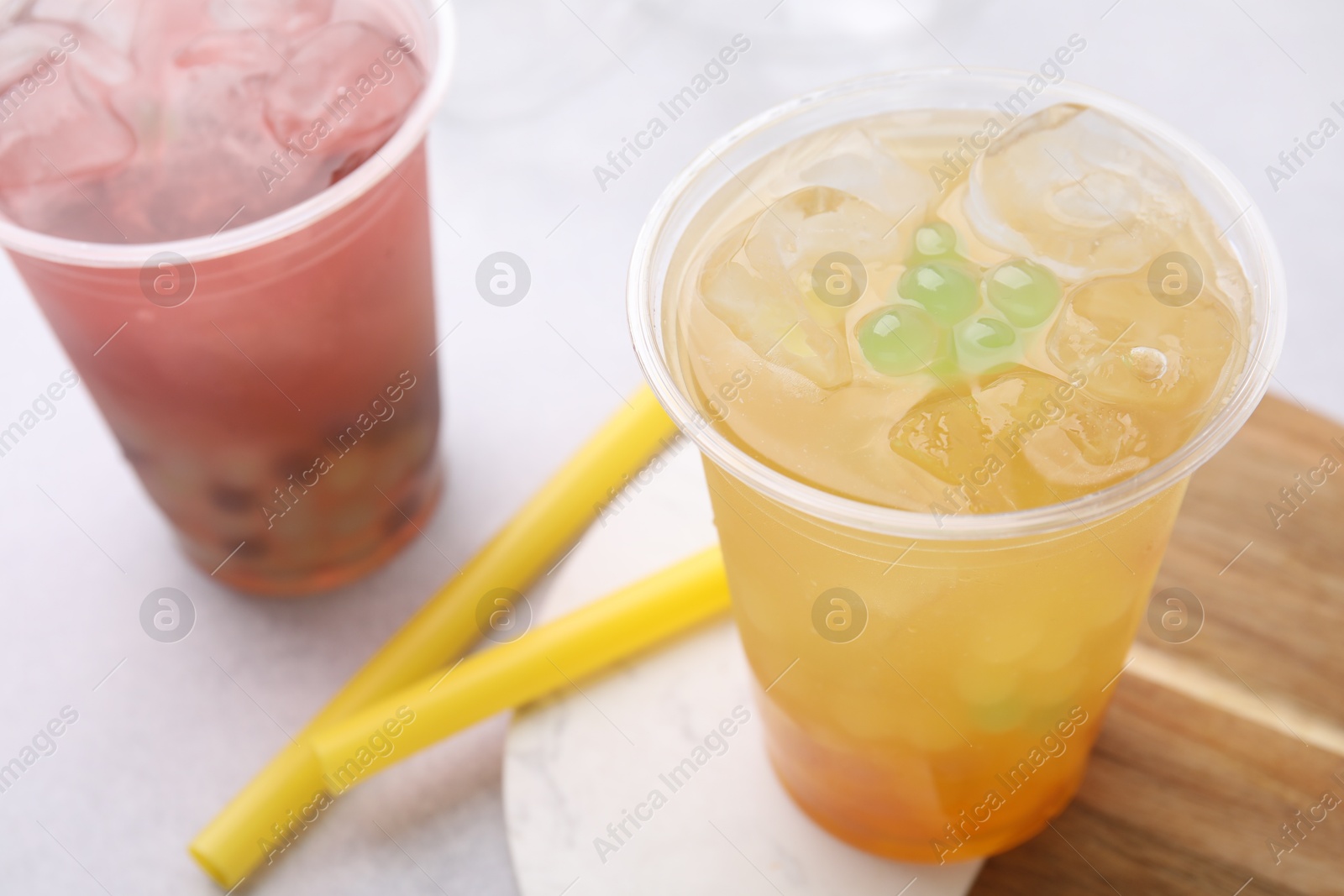 Photo of Tasty bubble tea in plastic cups and straws on light table, closeup