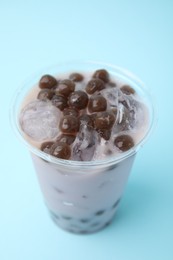 Photo of Tasty milk bubble tea in plastic cup on light blue background, closeup