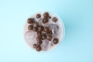 Photo of Tasty milk bubble tea in plastic cup on light blue background, top view