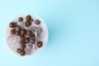 Photo of Tasty milk bubble tea in plastic cup on light blue background, top view. Space for text