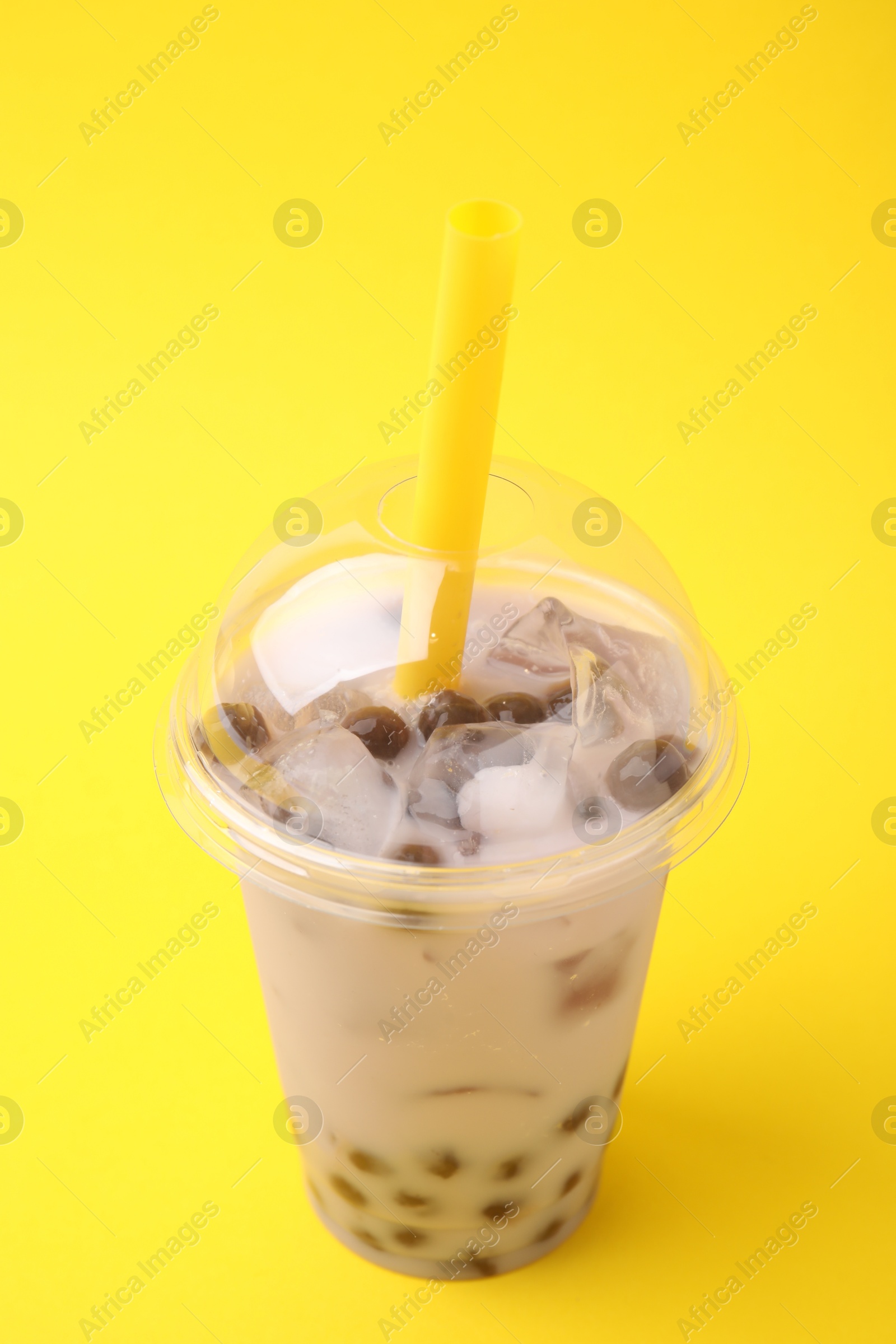 Photo of Tasty milk bubble tea in plastic cup on yellow background, closeup