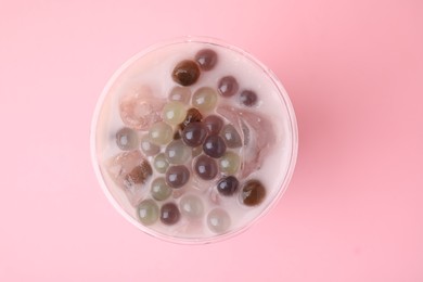 Photo of Tasty milk bubble tea in plastic cup on pink background, top view