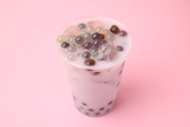 Photo of Tasty milk bubble tea in plastic cup on pink background, closeup