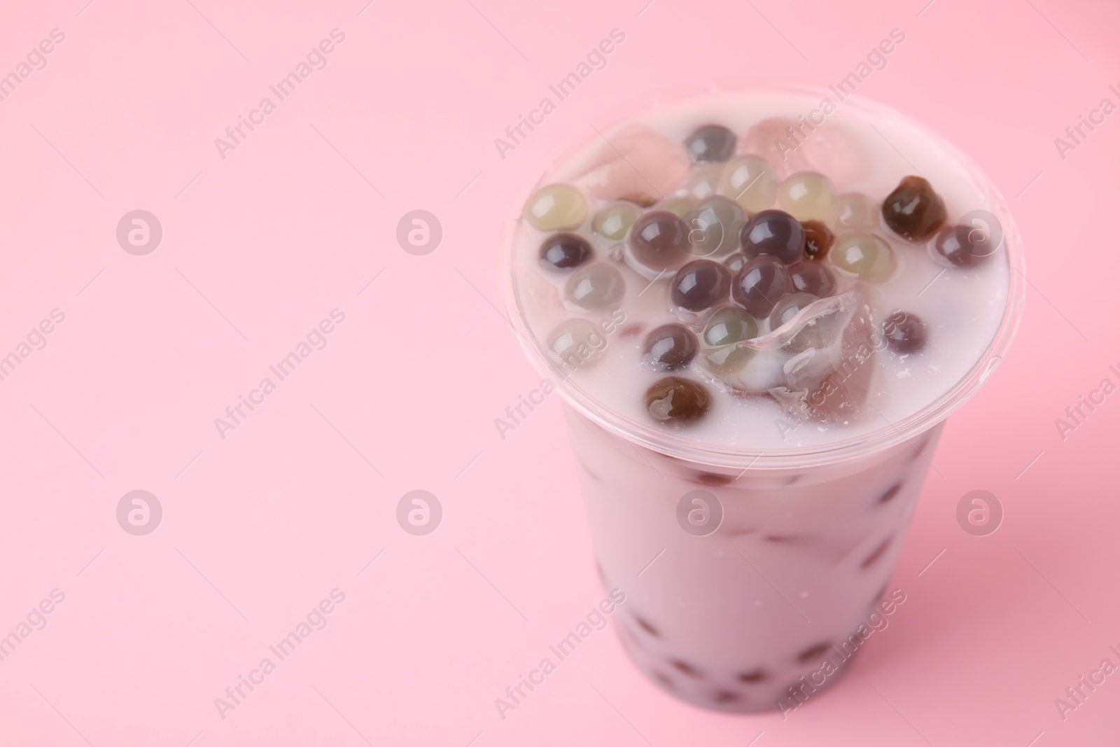 Photo of Tasty milk bubble tea in plastic cup on pink background, closeup. Space for text