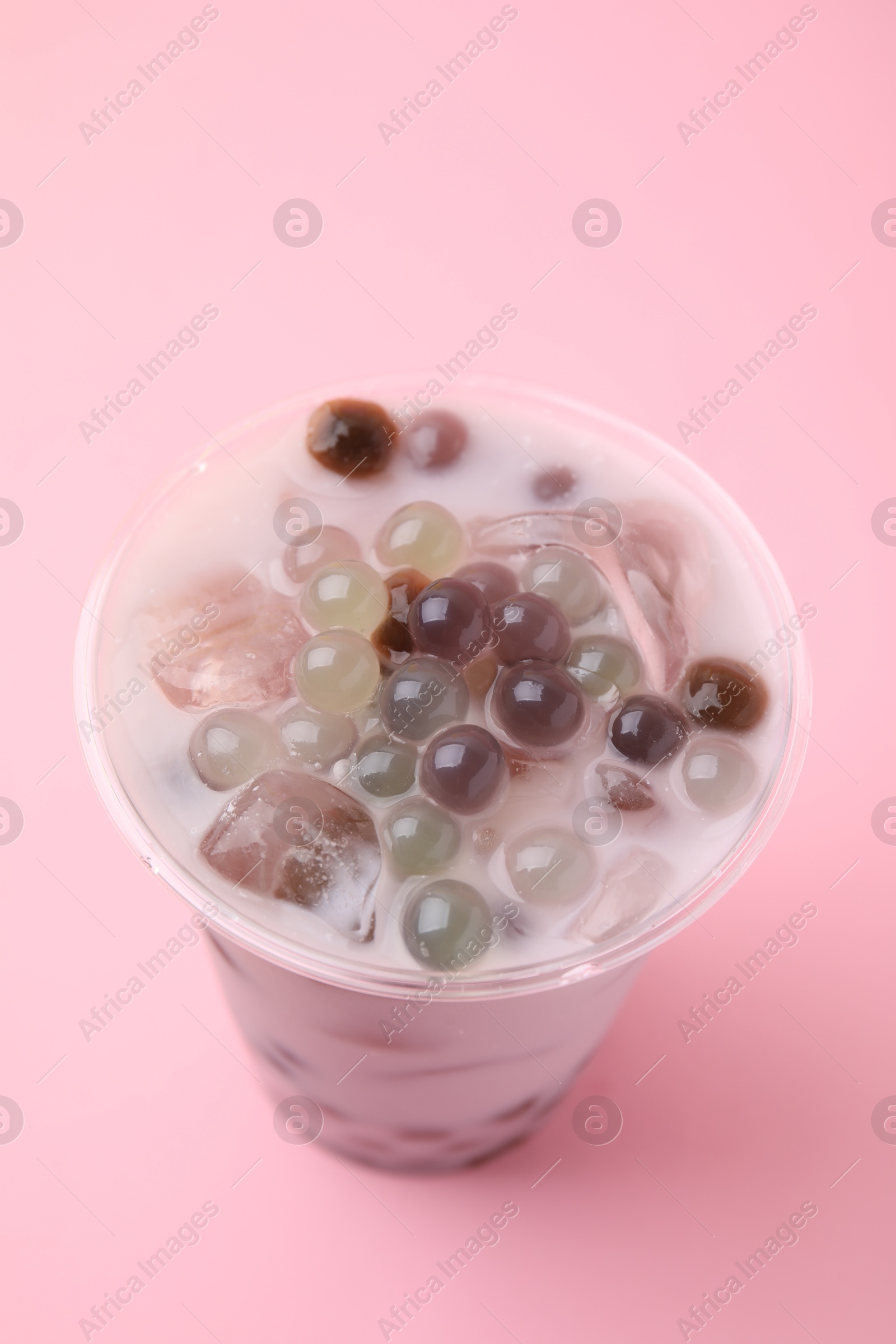 Photo of Tasty milk bubble tea in plastic cup on pink background, closeup