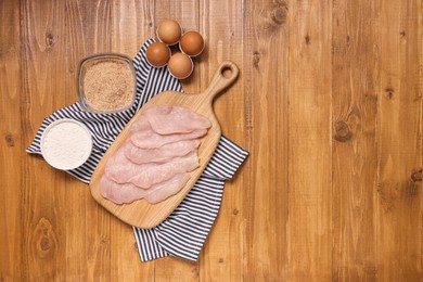 Cooking schnitzel. Raw meat, flour, eggs and breadcrumbs on wooden table, top view. Space for text