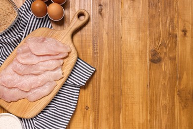 Photo of Cooking schnitzel. Raw meat, flour, eggs and breadcrumbs on wooden table, top view. Space for text