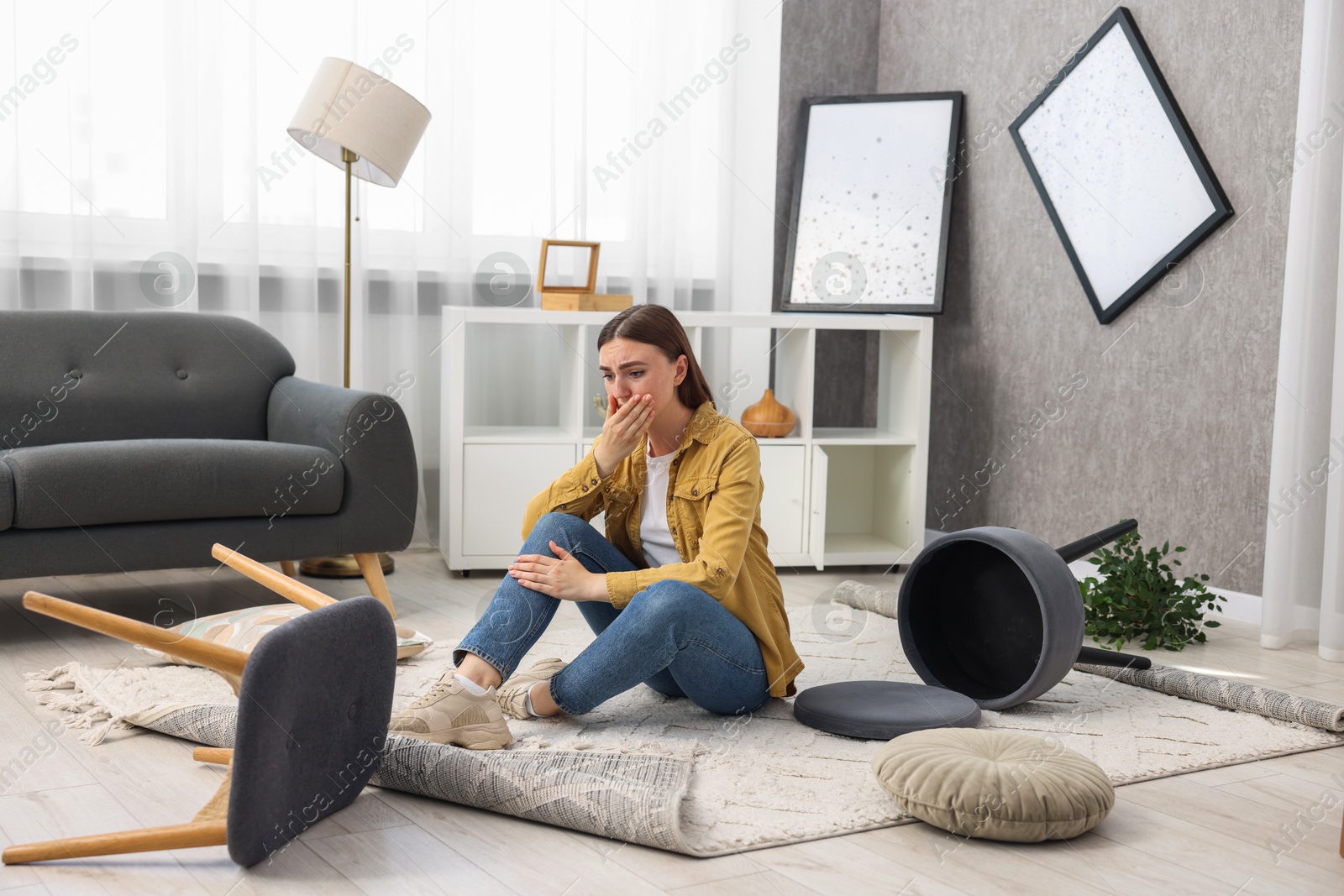 Photo of Desperate woman sitting on floor in messy living room after robbery