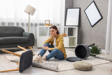 Desperate woman sitting on floor in messy living room after robbery