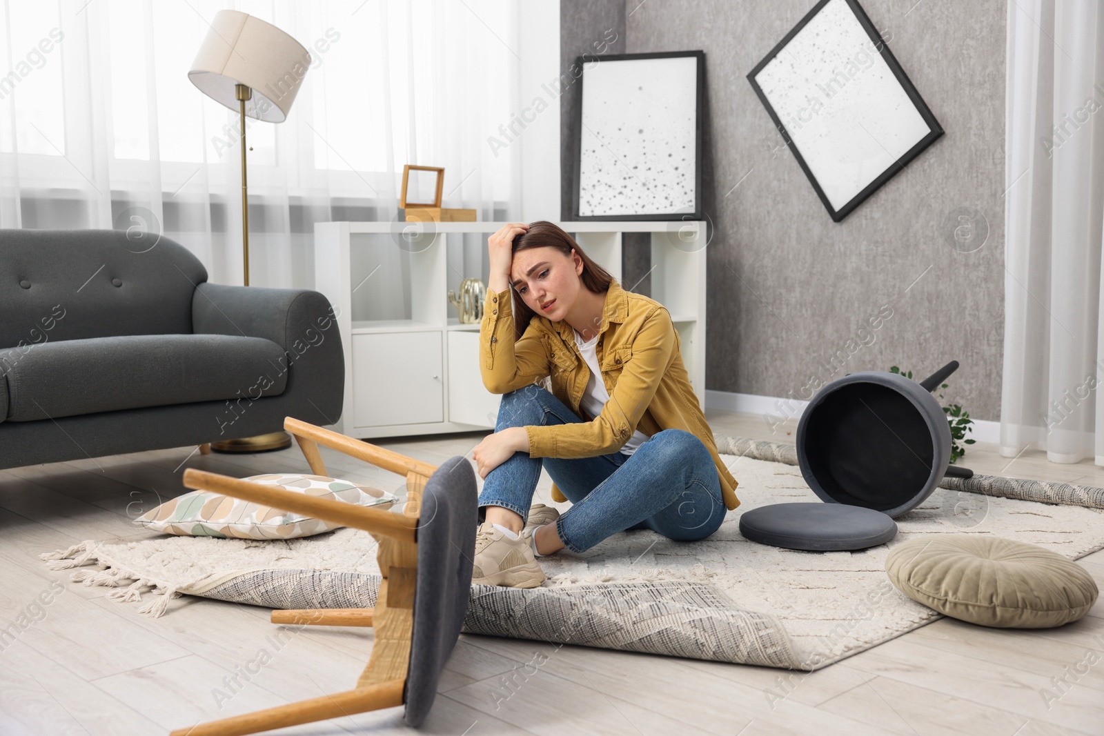 Photo of Desperate woman sitting on floor in messy living room after robbery