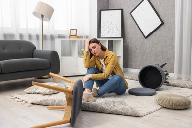 Photo of Desperate woman sitting on floor in messy living room after robbery