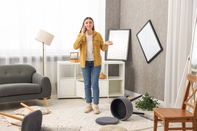 Desperate woman talking on smartphone in messy living room after robbery