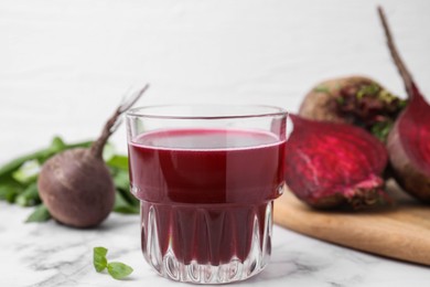 Photo of Fresh beet juice in glass and ripe vegetables on white marble table, closeup