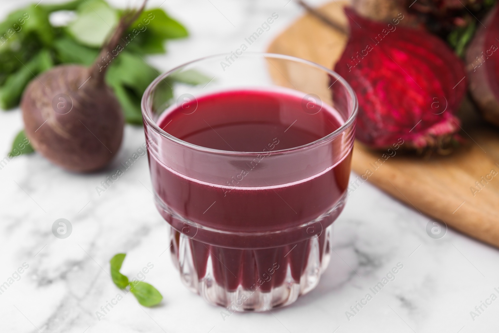 Photo of Fresh beet juice in glass and ripe vegetables on white marble table, closeup