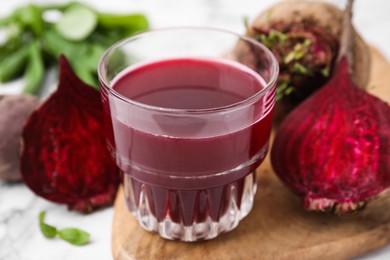 Photo of Fresh beet juice in glass and ripe vegetables on table, closeup